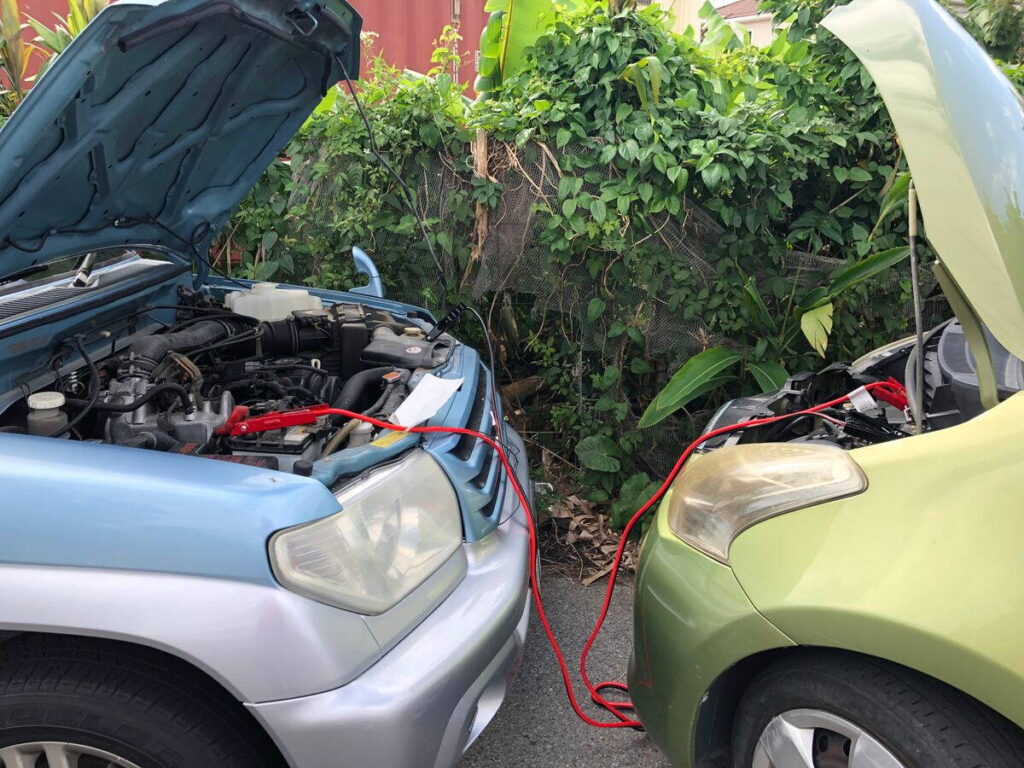 Két autó indítókábellel összekötve egy parkolóban