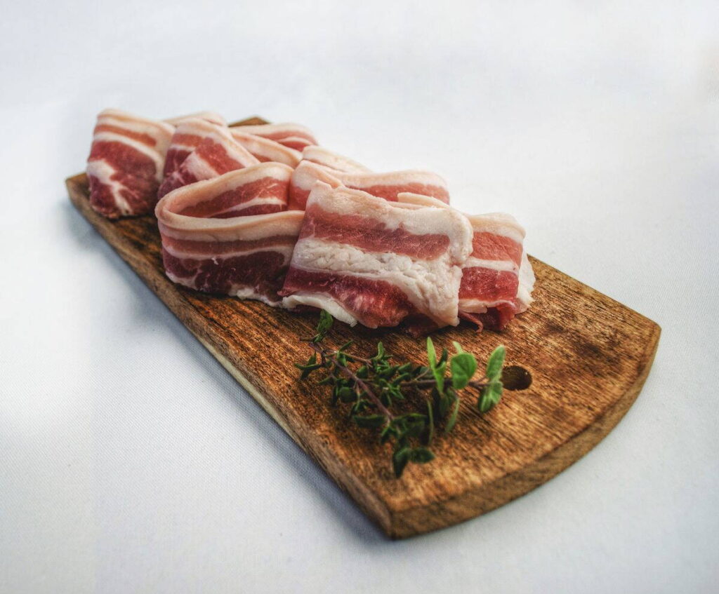 Szeletelt szalonna fűszerekkel egy fa deszkán