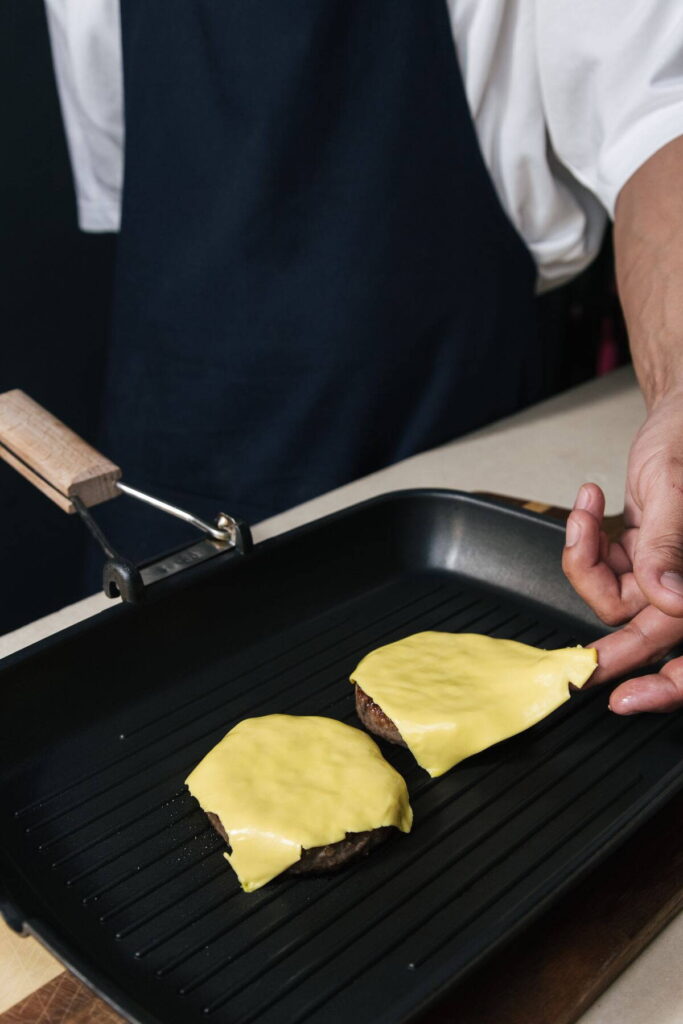 Sajtos hamburgerek sülnek egy tapadásmentes serpenyőben