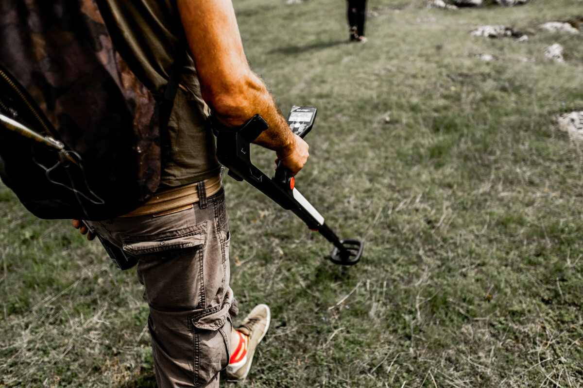 Fémkeresővel kutató ember egy füves mezőn