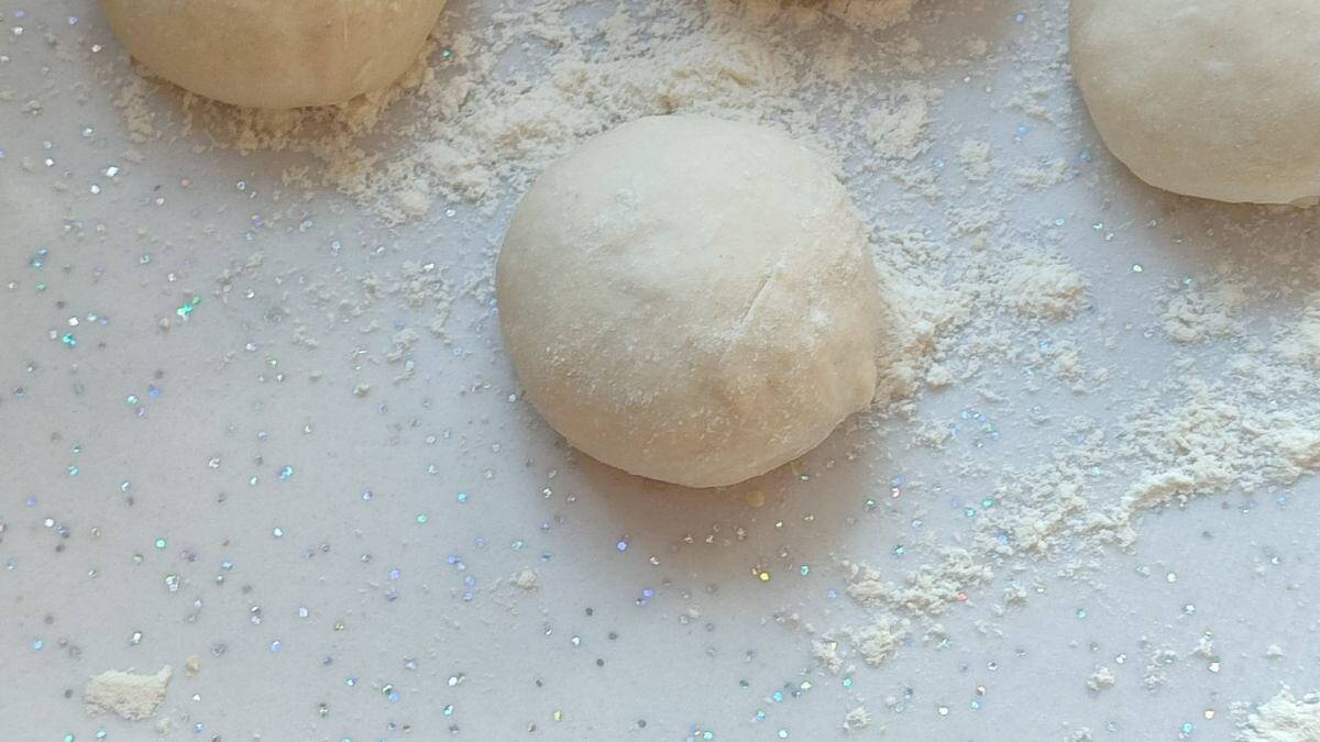Lisztes deszkán pihenő pizzatészta-golyók